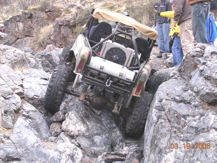 Tube-chassis rock buggy with rear radiator climbing jagged granite as spectators watch