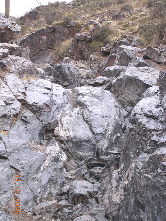 Steep jagged gray rock chute in a desert canyon with scrub brush above