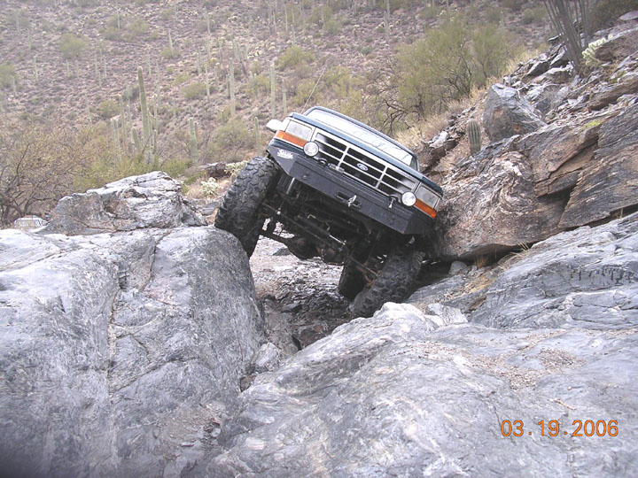 Lifted Ford 4x4 crawling down a rock ledge in saguaro desert, front view