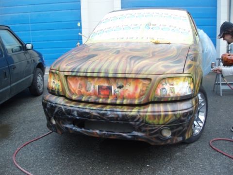1985 Ford Bronco II - A person airbrushes a custom flame design onto the front of a Ford F-150, with another vehicle parked to the left.
