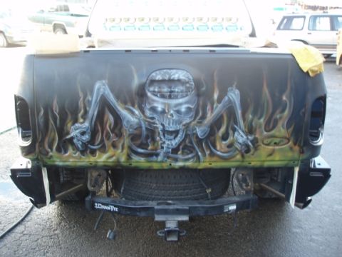 1985 Ford Bronco II - This custom tailgate features a striking airbrushed design of a skull emerging from flames, with a spare tire mounted below.
