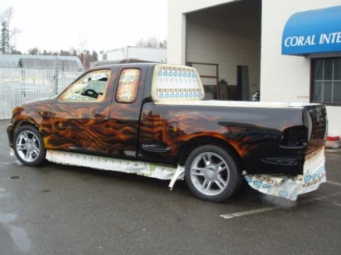1985 Ford Bronco II - Custom black pickup truck features flame graphics and aftermarket wheels, parked outside a building.