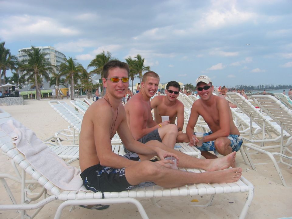Four guys relaxing on beach chairs with palm trees and buildings in the background