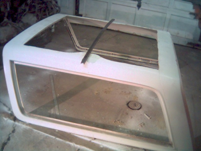 White fiberglass hardtop with glass windows sitting upside down on a garage floor