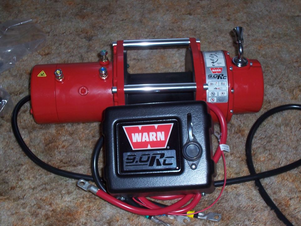 Red WARN 9.0Rc winch with its black control pack and red power cables laid out in front on carpet