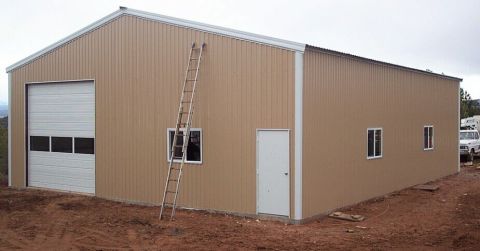 1986 Ford Ranger - A tan metal building with a large overhead garage door and a ladder leaning against the side wall. A white truck is visible to the right.