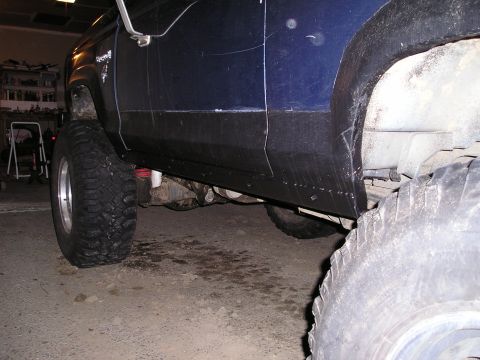 1986 Ford Bronco II - The side panel and fender flare of a blue SUV are visible, showing off its lifted suspension and large tires.