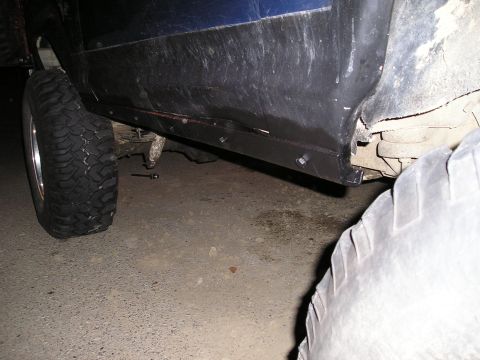 1986 Ford Bronco II - Close-up of a vehicle's side panel and undercarriage, showing a large tire and black trim.