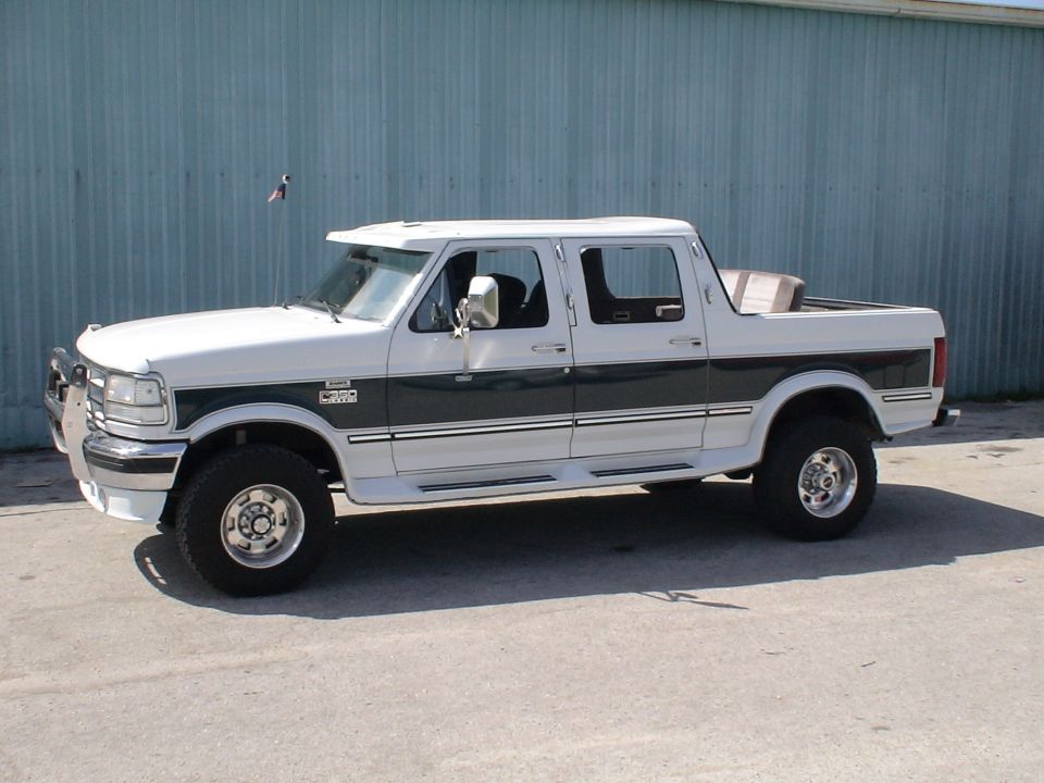 White and green crew cab Ford pickup in side view, lifted with chrome brush guard