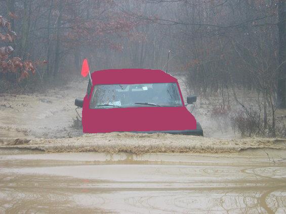 Red SUV driving through muddy water with a red flag on top