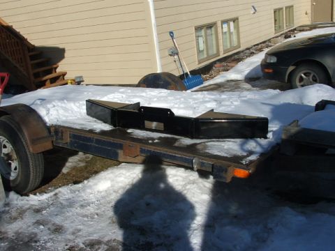 1990 Chevrolet Suburban - A black bumper part is resting on a trailer covered in snow, with a house and a car visible in the background.