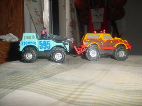 1988 Ford Bronco - A toy tow truck tows a toy SUV. The tow truck has 'STOMPER 595' on its side.