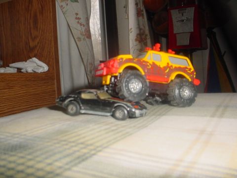 1988 Ford Bronco - Two toy vehicles are positioned on a checkered surface, with a wooden cabinet and curtains in the background.