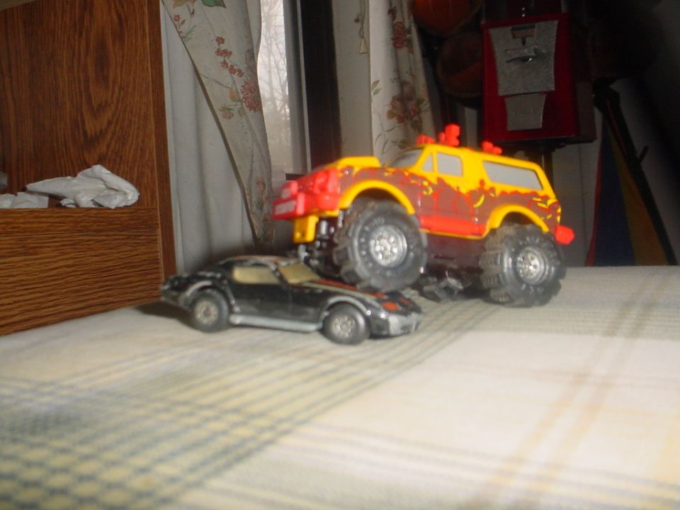 Toy monster truck on top of a toy sports car