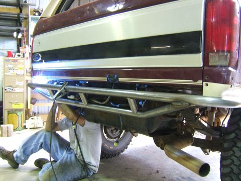 1993 Ford Bronco - A person welds a custom rear bumper onto a maroon and white Ford Bronco in a workshop.