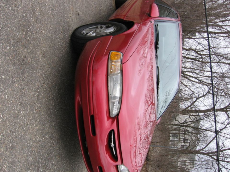 Red car front quarter view. The grille and headlight shape suggest a mid-1990s vehicle