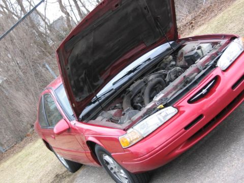 1995 Ford Thunderbird - The engine bay of a red 1995 Ford Thunderbird is visible with the hood raised.