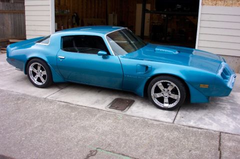 1979 Pontiac Trans Am - This blue 1979 Pontiac Trans Am features a distinctive body style and aftermarket chrome wheels, seen parked outside a garage.