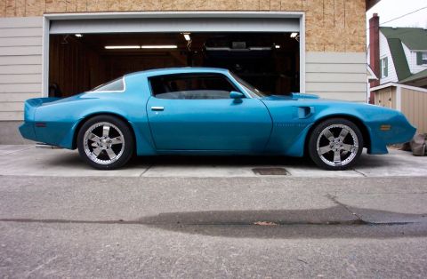 1979 Pontiac Trans Am - A blue coupe with custom wheels is parked in front of a garage.