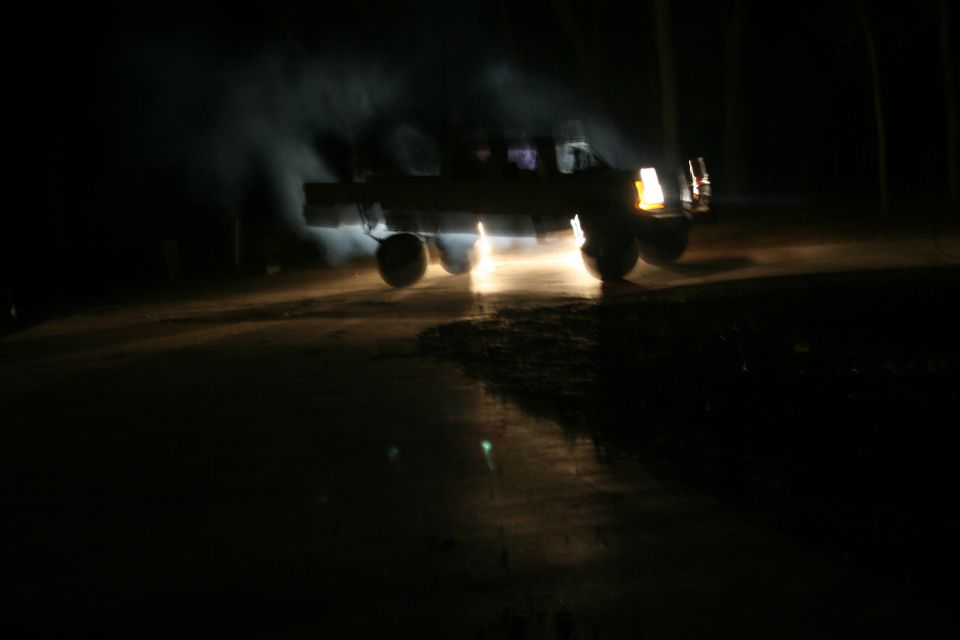 Dark night shot of a lifted truck on a dirt road, headlights flaring and dust kicked up