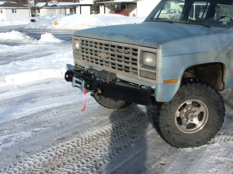 1990 Chevrolet Suburban - A light blue pickup truck with a winch and off-road tires is parked on a snowy road.