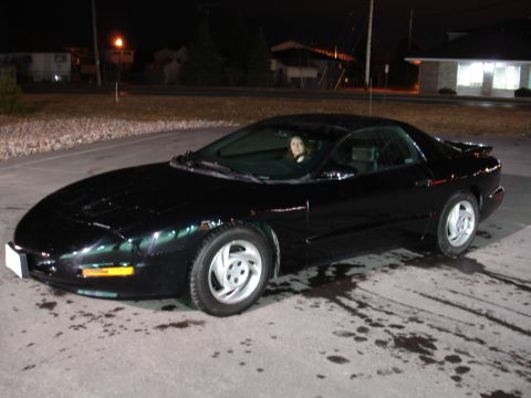 1981 Ford Mustang - A black Pontiac Firebird is parked outside a building at night with a person inside.