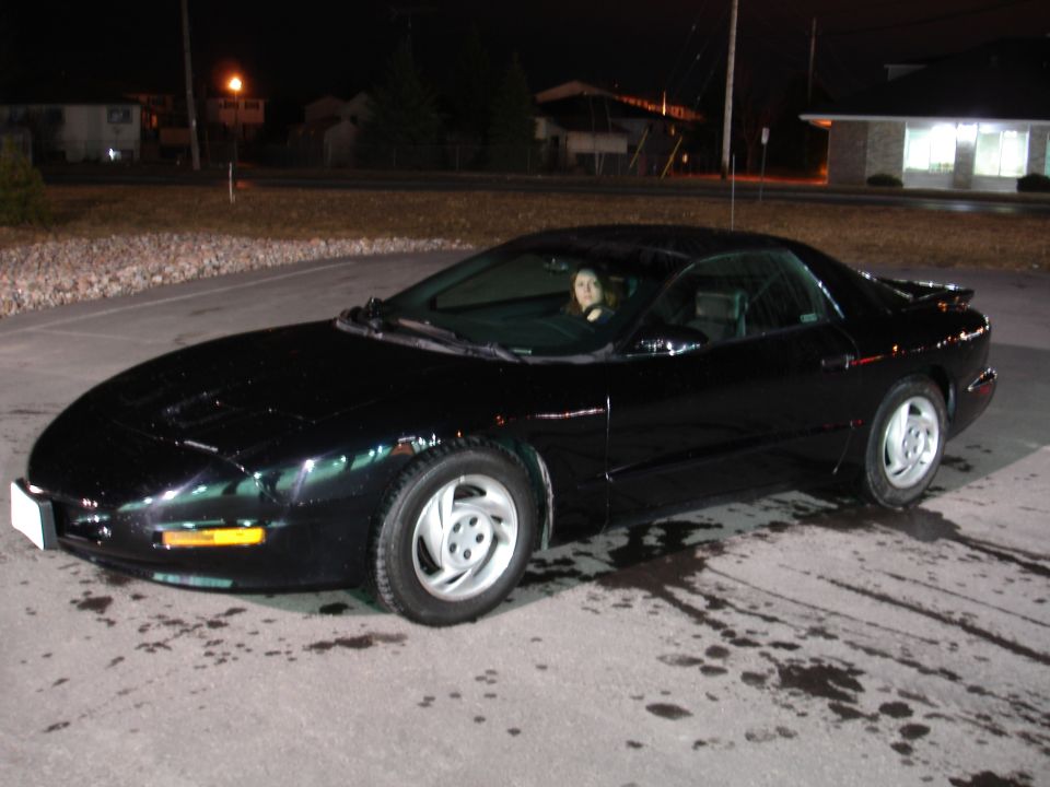 black Pontiac Firebird parked at night, woman in driver's seat