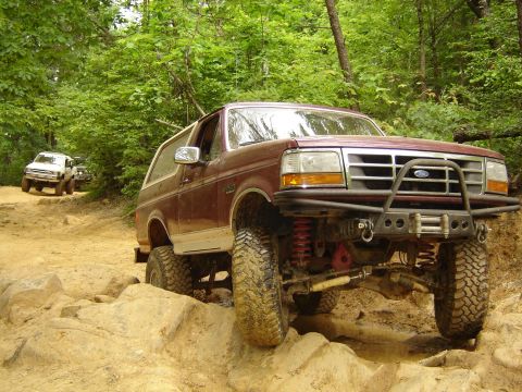 1993 Ford Bronco - This modified Ford Bronco is tackling a challenging off-road course with other vehicles in the background.