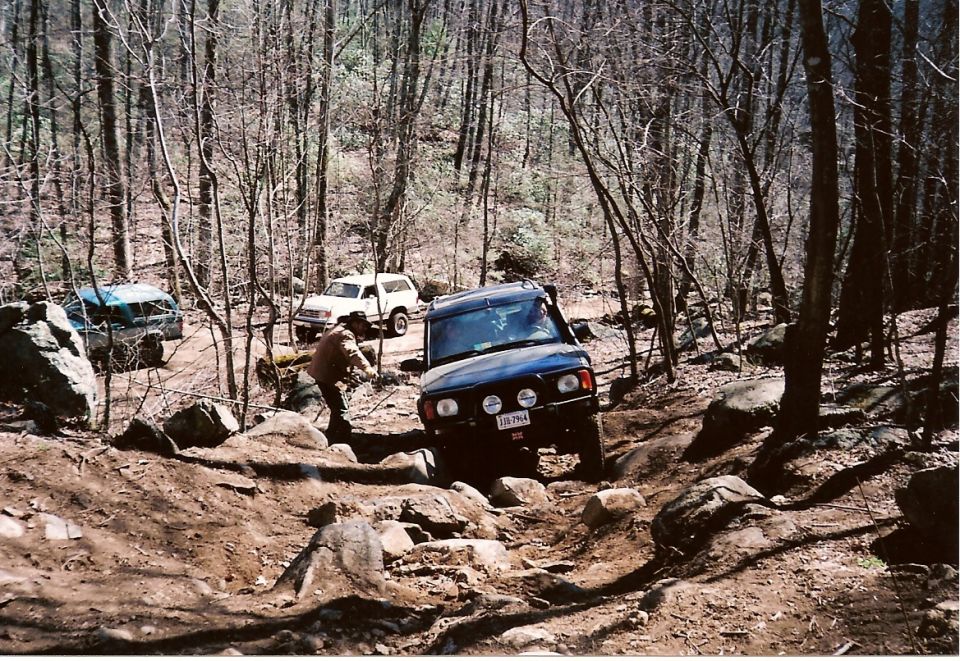 Dark blue SUV navigates rocky terrain with two other SUVs behind it