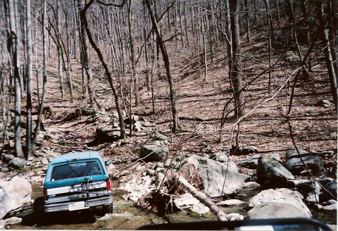 1987 Ford Bronco - Teal and white 1987 Ford Bronco navigates a rocky stream during an off-road excursion.