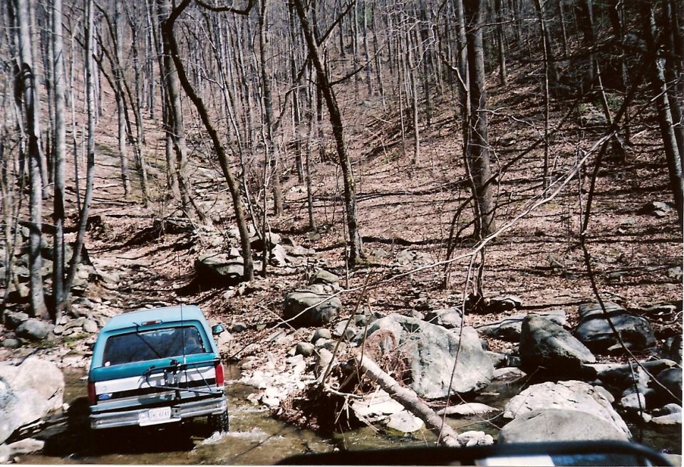1987 Ford Bronco rear view, teal and white, driving off-road