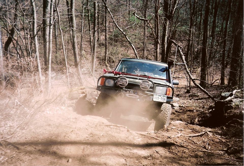 Dark SUV with Hella lights, brush guard and snorkel climbing a dusty forest trail, plate 089-DSR