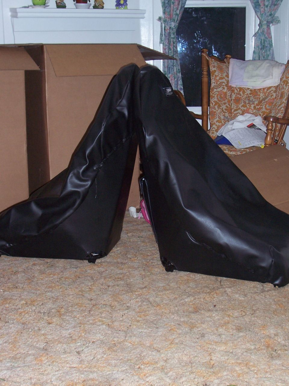 Two black car seats covered in plastic bags, leaning against each other indoors