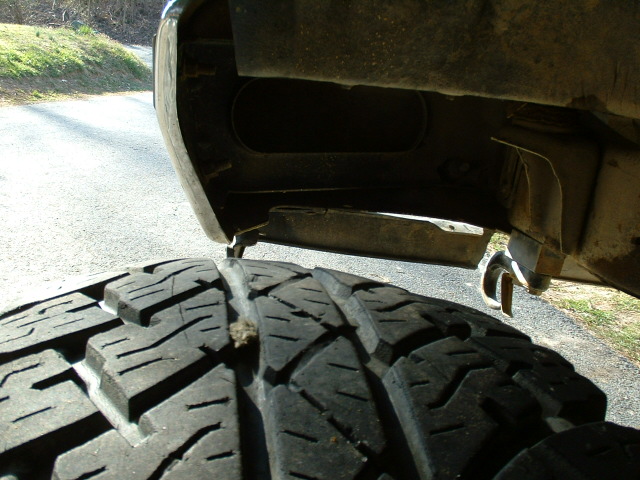 Close-up of all-terrain tire center tread held in front of a truck's underbody