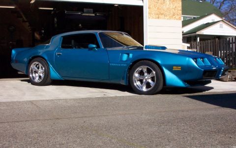 1979 Pontiac Trans Am - A blue 1979 Pontiac Trans Am with chrome wheels is parked in front of a garage.