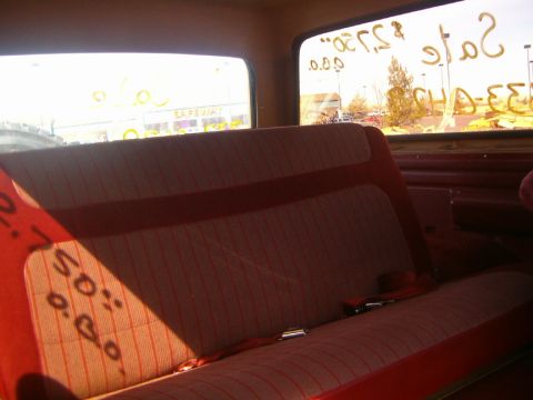 1985 Ford Bronco - The interior of a vehicle shows a red and white striped bench seat with a red seatbelt. Writing is visible on the windows.