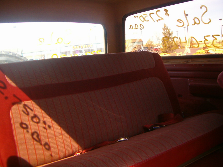 Interior shot of a vehicle's back seat, looking out the windows. Windows have yellow writing on them, including 'Sale' and numbers