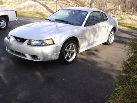 1998 Ford Taurus - Silver coupe with a black grille and chrome wheels, parked on asphalt next to a white pickup truck.