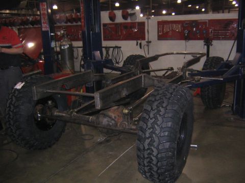 1978 Ford Bronco - The chassis of a vehicle is suspended in a workshop, with large tires and exposed frame components visible.
