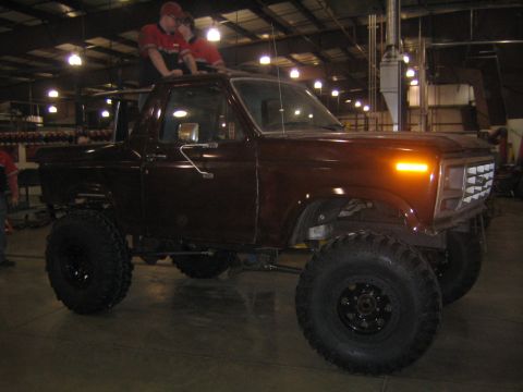 1978 Ford Bronco - This lifted Ford Bronco has oversized tires and is parked inside a garage with two people on its roof.
