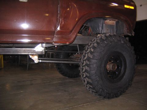 1978 Ford Bronco - The side profile of a brown 1978 Ford Bronco is visible, highlighting its off-road tires and suspension modifications.