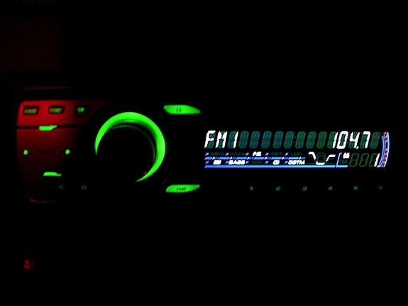 Aftermarket car stereo head unit lit up showing FM 104.7 display