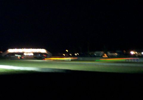 1979 Ford F-150 - Motion blur captures the speed of vehicles on a track at night, illuminated by overhead lights.