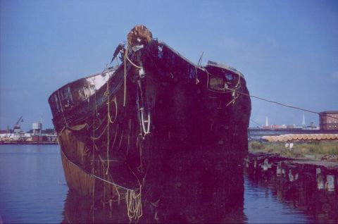 1988 Ford Bronco - A derelict ship sits in the water near a dock, with industrial structures visible in the distance.