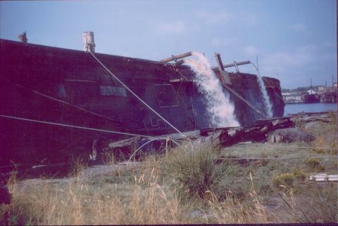 1988 Ford Bronco - Water flows from pipes on a large barge docked near a harbor with buildings in the background.