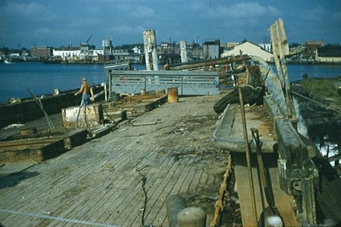 1988 Ford Bronco - A man stands on a weathered wooden deck overlooking a harbor with industrial buildings.