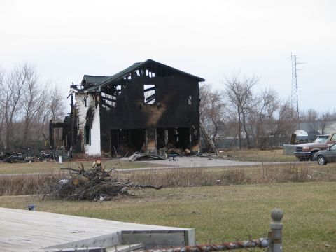 1994 Ford Bronco - A house is heavily damaged by fire, with a brown truck and a grey car visible in the background.