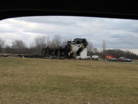 1994 Ford Bronco - A house is heavily damaged by fire, with multiple vehicles visible in the yard.
