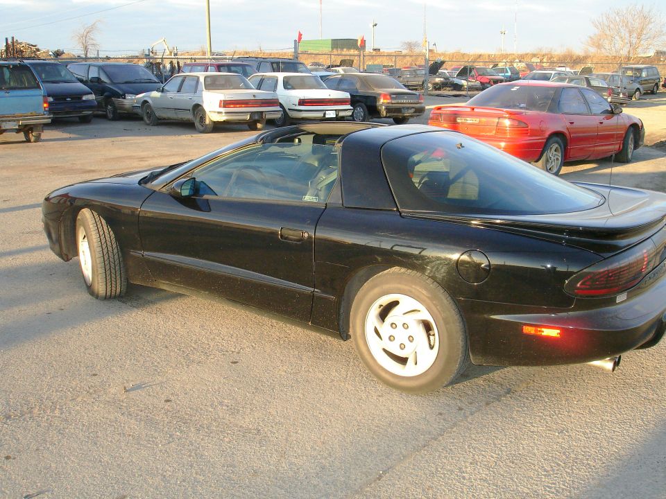Black sports car with a t-top roof and white five-spoke wheels, parked on asphalt