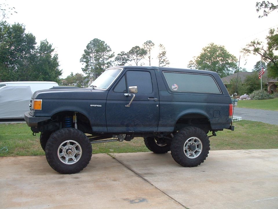 Lifted dark blue Ford Bronco on mud tires, side view on a concrete driveway
